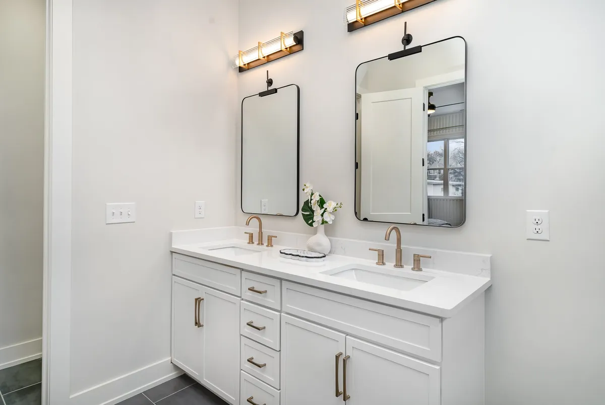 A luxurious bathroom with dual sinks, stylish mirrors, and chic light fixtures, complemented by a fresh flower arrangement. The mood is serene, inviting, and designed for shared morning routines or relaxing evening rituals.