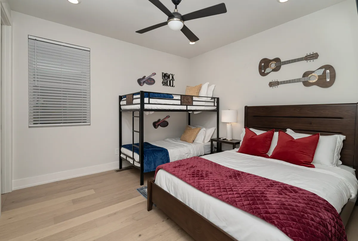 A vibrant bunk room featuring both bunk beds and a queen bed, with cheerful guitar-themed wall decorations and a colorful quilt. A nightstand with a lamp adds practicality and warmth, making it perfect for families or groups.