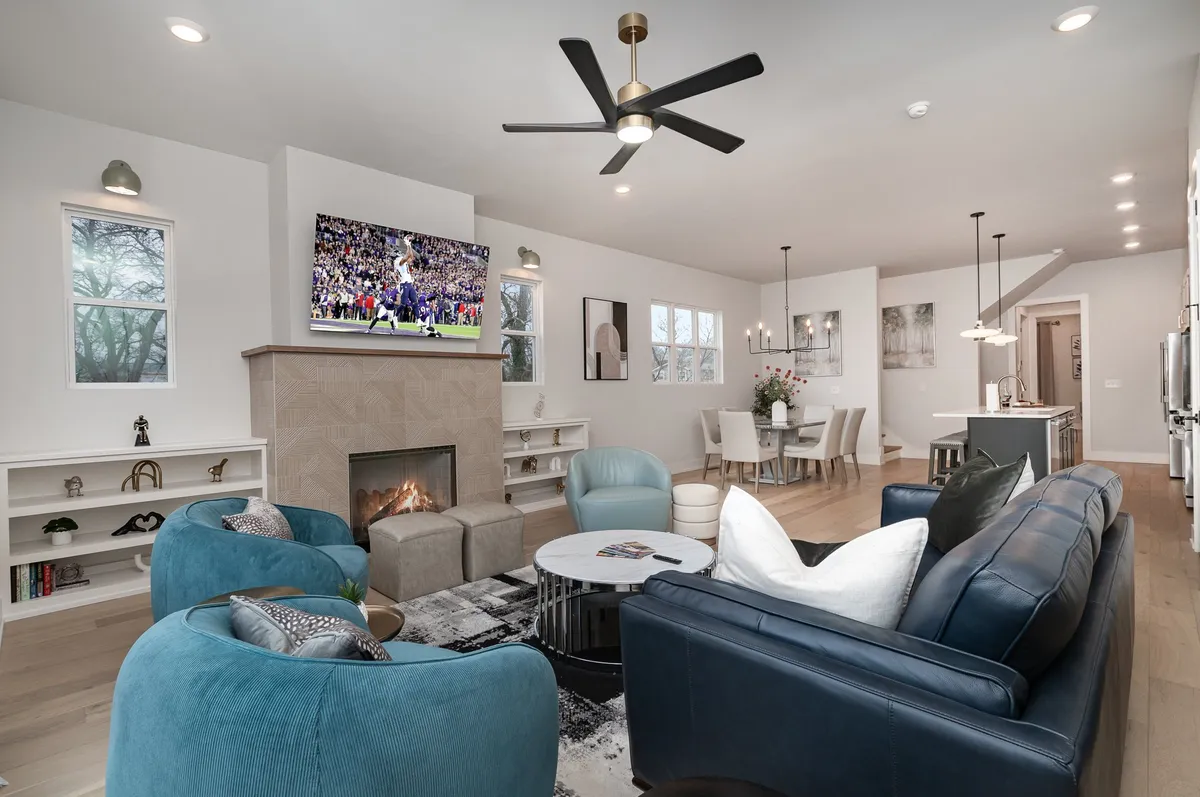 The image showcases a stylish, open-concept living and dining area with a cozy fireplace, large television, and ample comfortable seating—perfect for gathering with friends or family. The scene radiates a cheerful, lively atmosphere ideal for watching the big game, socializing, or relaxing during special occasions.