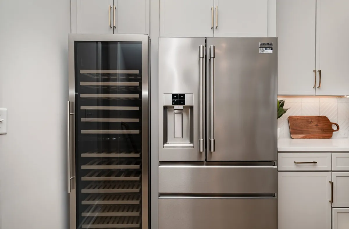 A modern kitchen scene featuring a stainless steel refrigerator, a wine cooler, and a wooden cutting board on the counter. The design is contemporary and welcoming, emphasizing both functionality and style for hosting and culinary adventures.