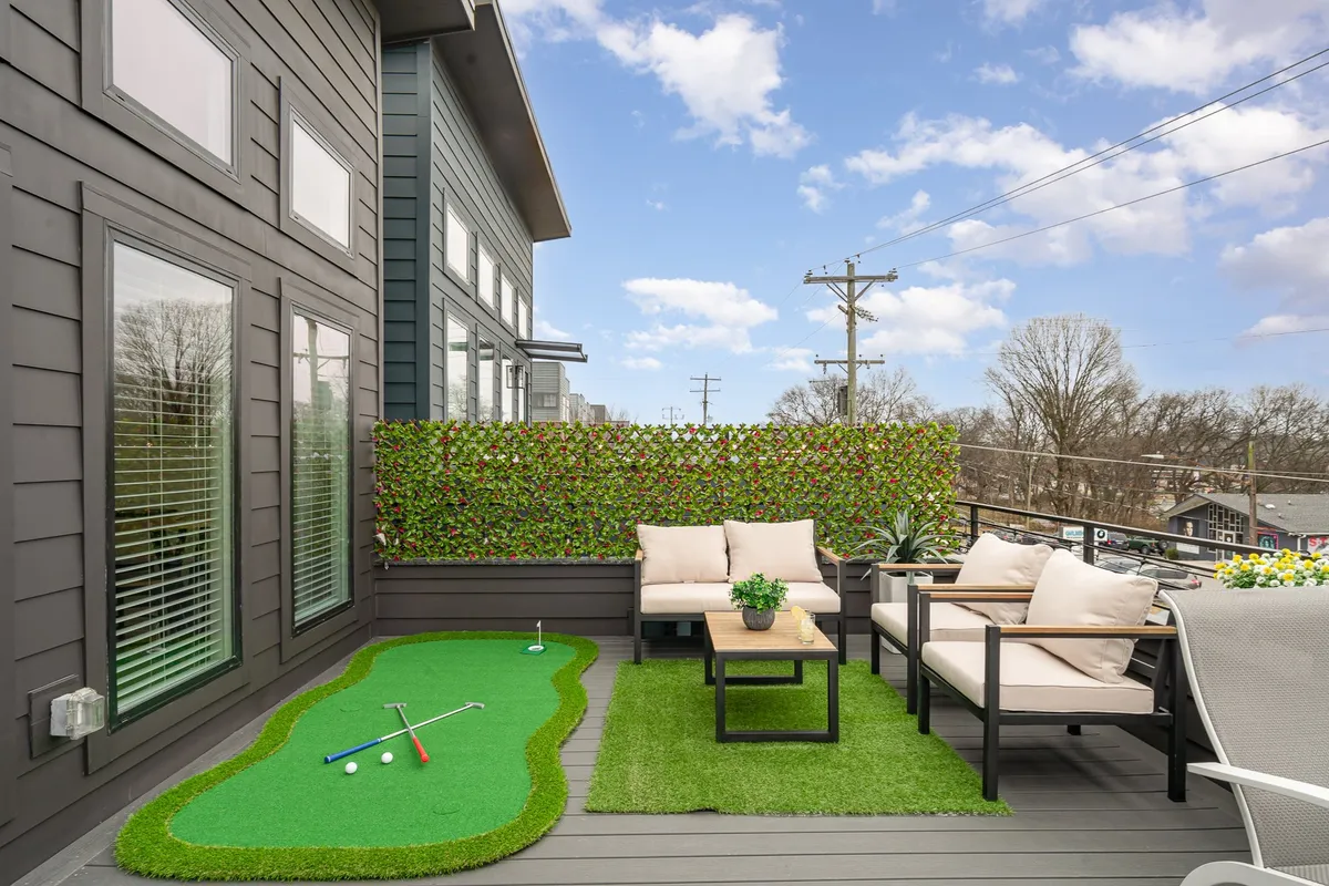 An inviting rooftop outdoor space featuring a putting green, comfortable seating, and lush potted plants. The area is bathed in natural light, hinting at sunset views and a relaxed, social atmosphere ideal for entertaining or unwinding.