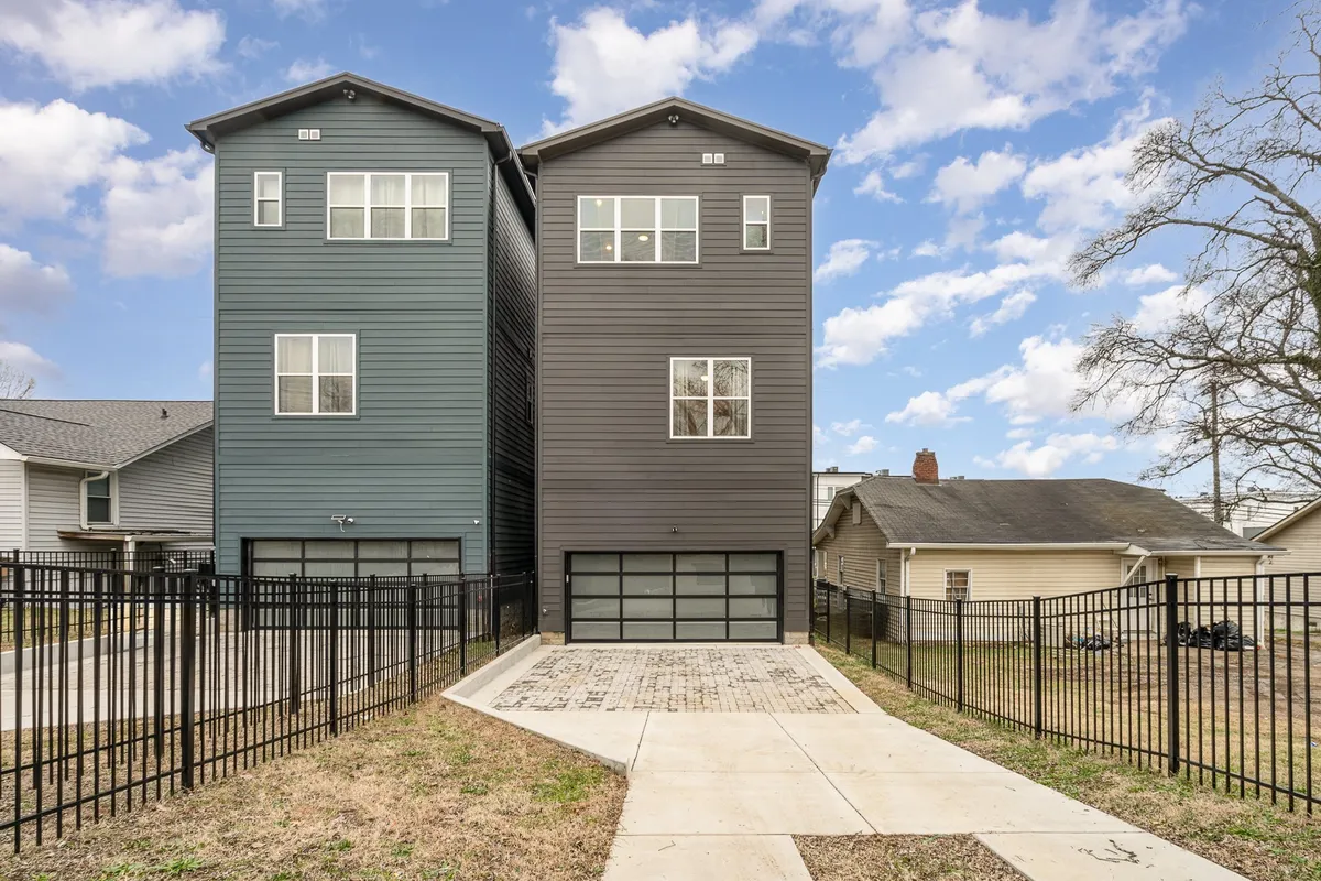 A welcoming exterior shot of two modern homes with a fenced driveway under a cloudy blue sky. The homes’ sleek, contemporary design hints at upscale living and group gatherings.