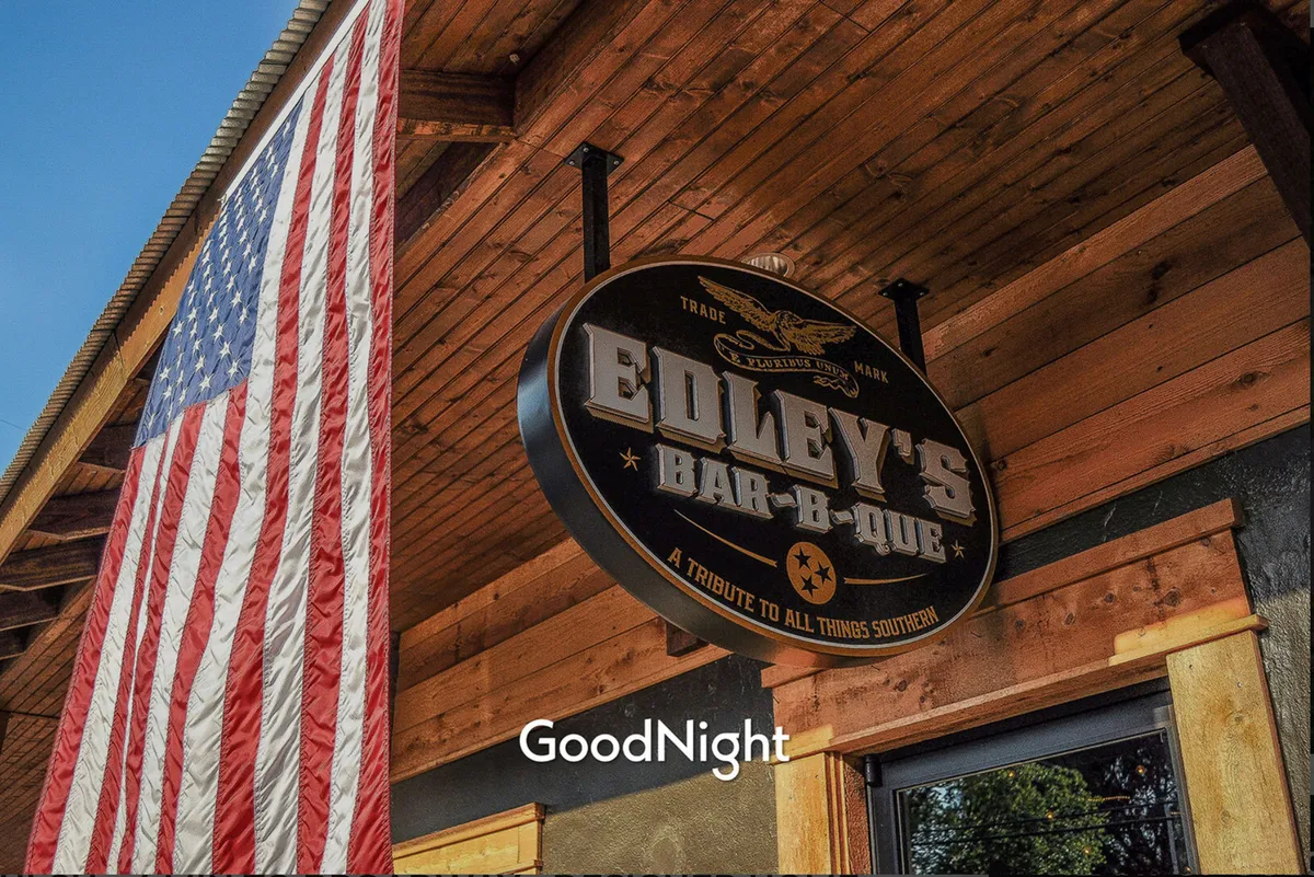An exterior view of Edley’s Bar-B-Que, with its iconic sign and a welcoming atmosphere. People are seen dining and socializing, capturing the communal and festive vibe of a beloved local hotspot.