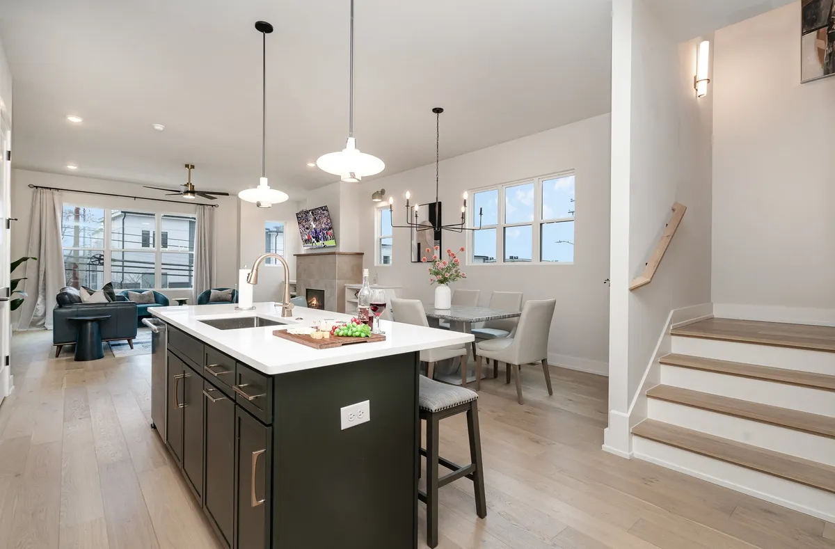 A spacious, open-plan interior with a kitchen island, dining table, living area, and a visible staircase. The setting is ideal for family meals, entertaining guests, and casual gatherings, combining kitchen, dining, and living spaces in one cohesive view.
