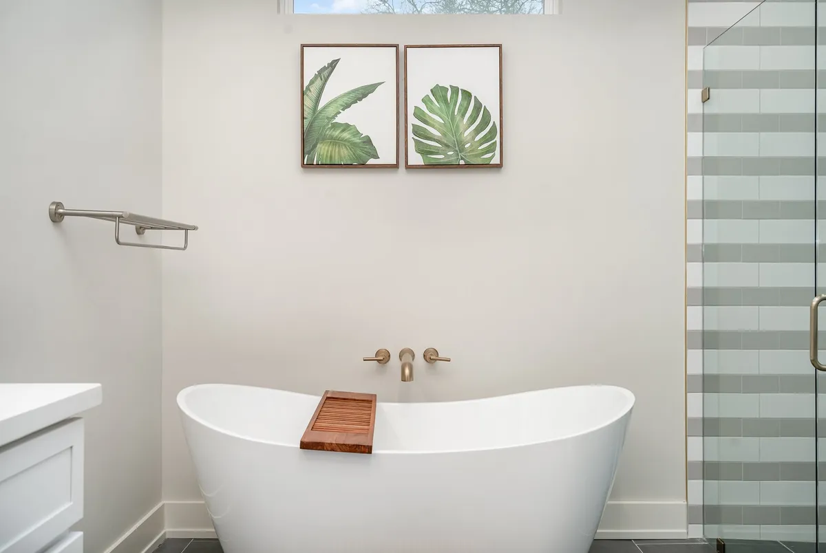 A tranquil bathroom sanctuary with a freestanding bathtub, framed leaf prints, a wooden bath tray, and a separate shower area. The space evokes calm and relaxation—ideal for personal self-care routines and quiet moments.