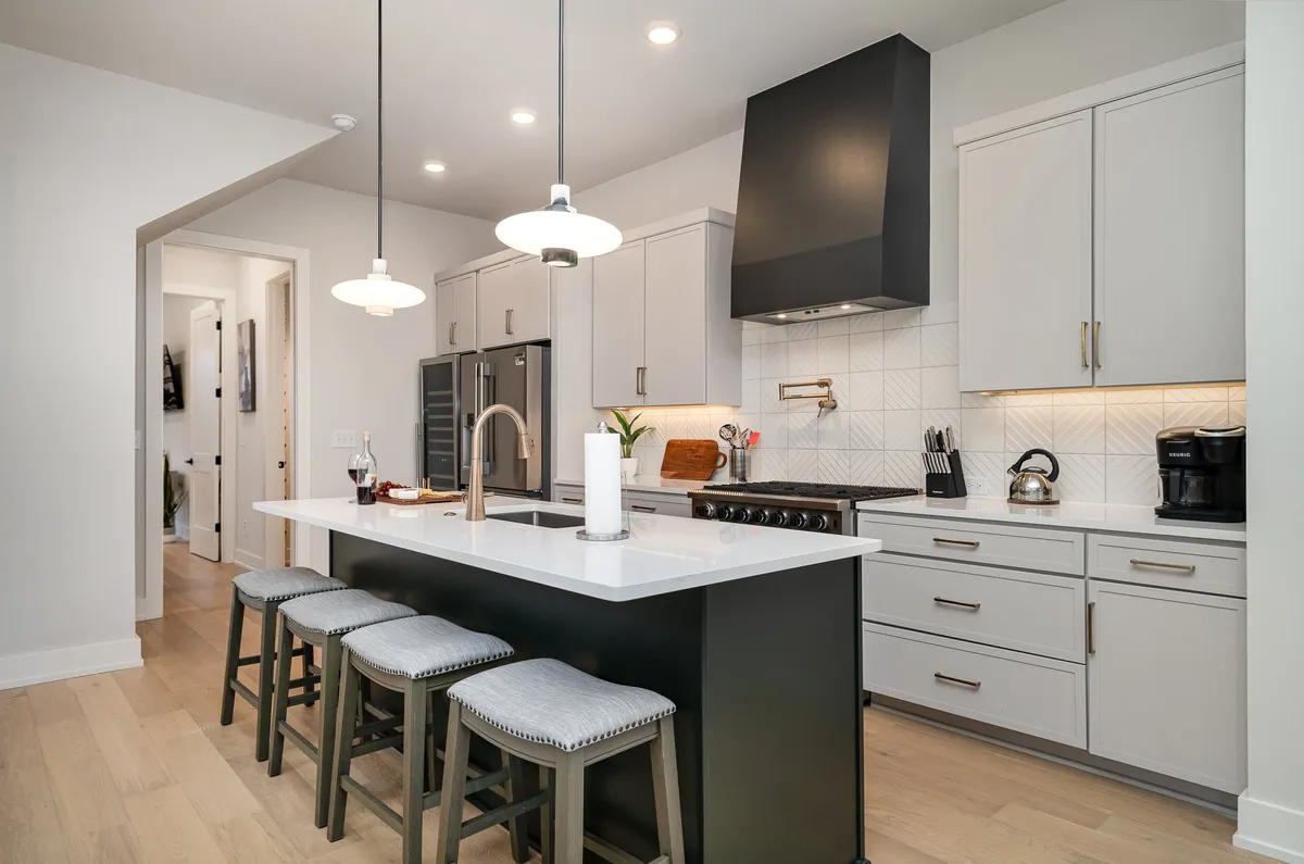 A bright, inviting kitchen featuring a central island, sleek appliances, and stylish lighting. The space is designed for cooking, dining, and gathering, with amenities visible on countertops.