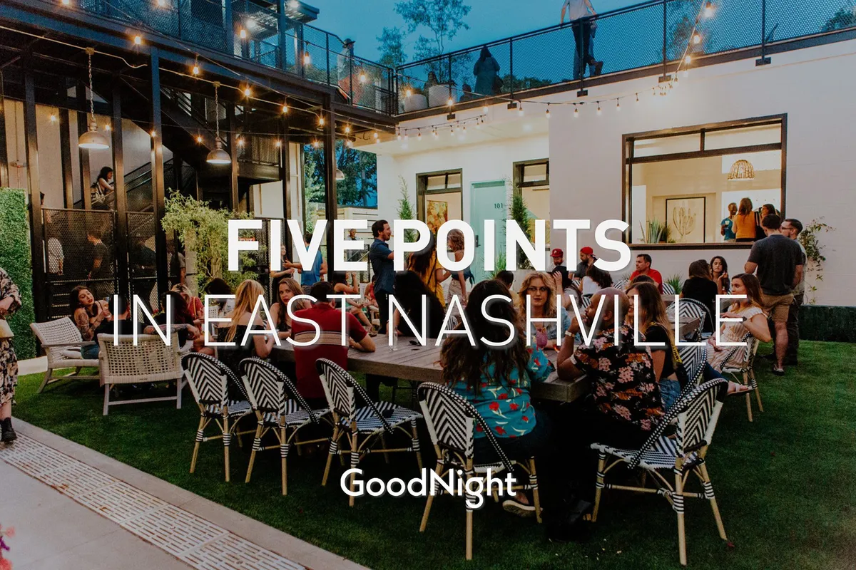 An exterior scene featuring people socializing around a dining table beneath string lights, with modern architecture in the background. The mood is lively and joyful, suggesting a space ideal for outdoor gatherings, group celebrations, or networking events.